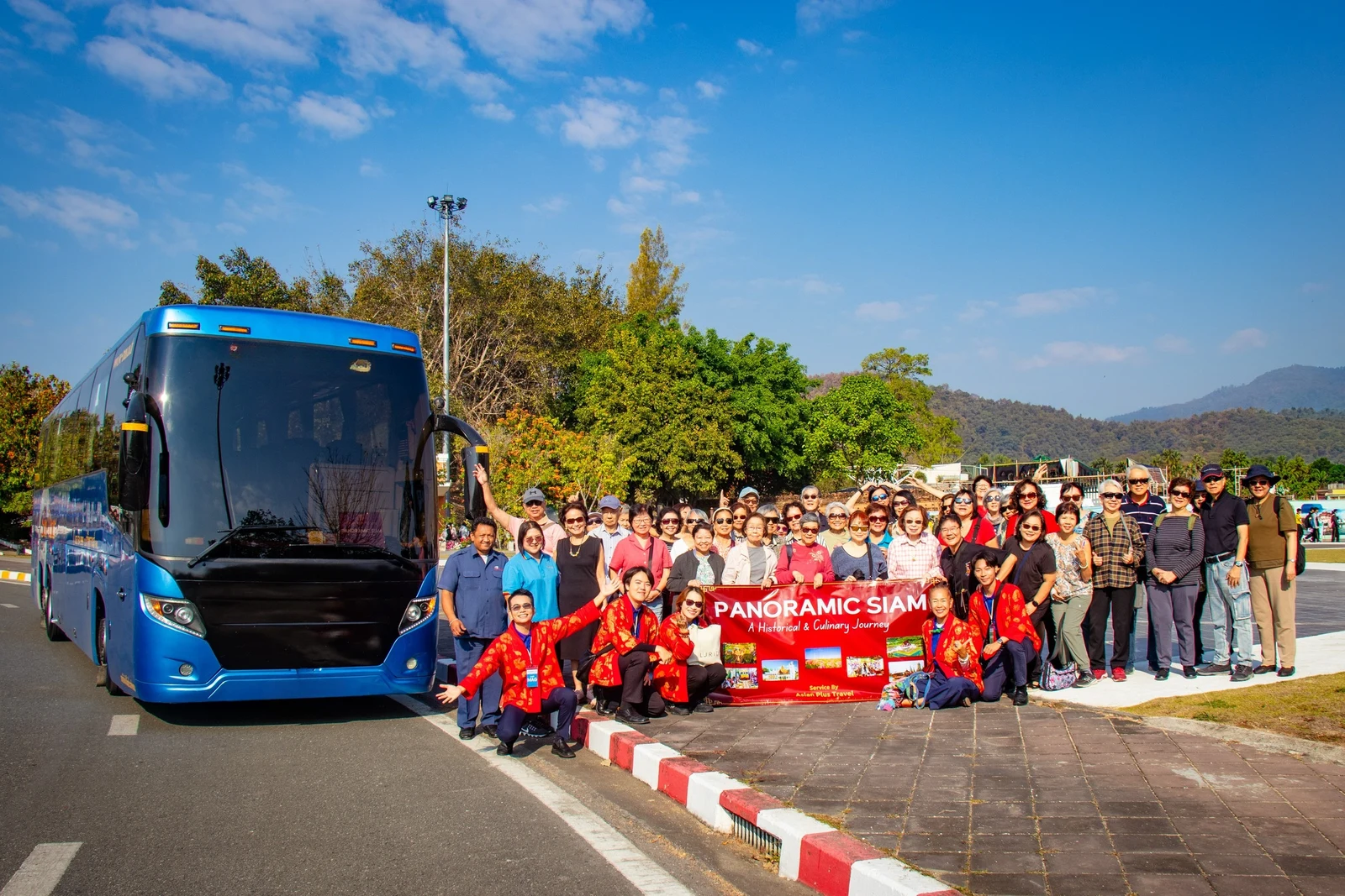 APT team and travelers beside a blue tour bus during the Panoramic Siam group trip