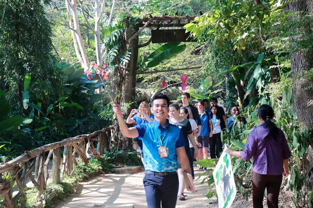 Phudit leading a group of travelers along a tree-lined walkway